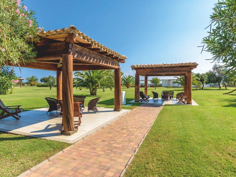 Zwei Holzpergolen mit Sitzgelegenheiten neben einem Pool auf einer gepflegten Rasenfläche bei klarem Himmel.
