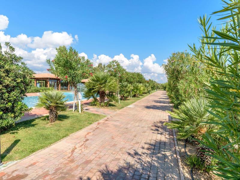 Gepflasterter Weg neben Grünflächen und Pool unter blauem Himmel mit Wolken.