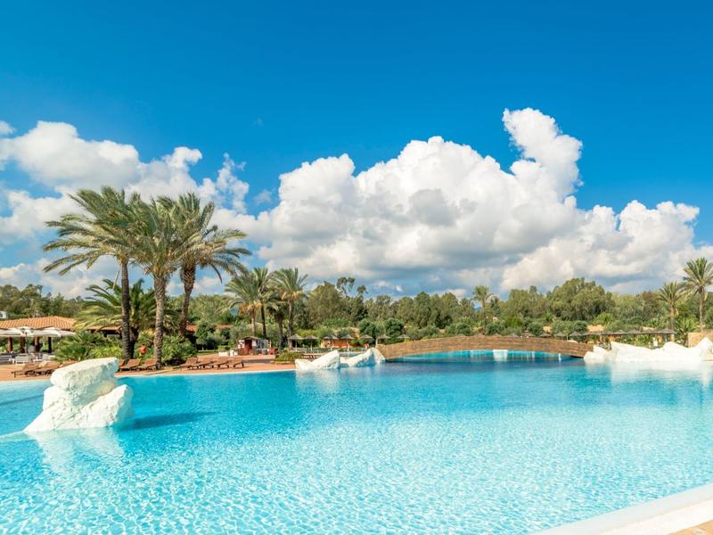 Großer Pool mit klarem Wasser, Palmen und blauem Himmel mit Wolken.