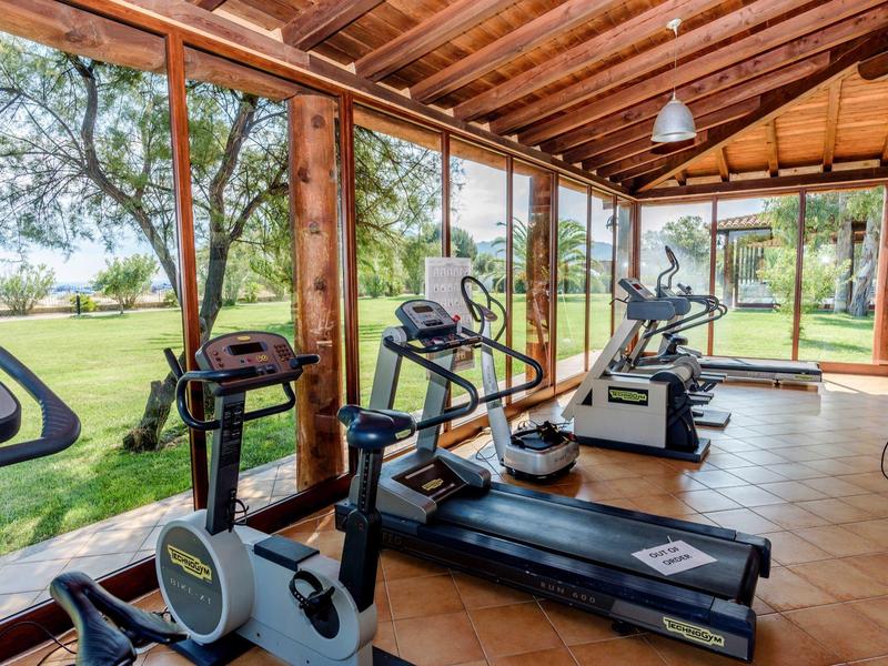 Fitnessraum mit Holzbalkendecke und großen Fenstern mit Blick auf die Gartenlandschaft.