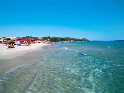 Klarer Strand mit weißem Sand, Sonnenschirmen und ruhigem, blauem Meer unter klarem Himmel.