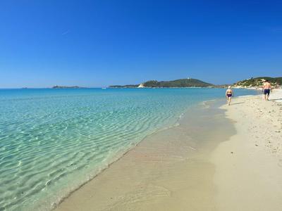 Ciel bleu clair au-dessus d'une plage de sable calme et en pente douce avec quelques personnes.