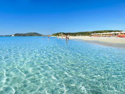 Mer turquoise claire avec plage de sable blanc et côte étendue sous ciel bleu.
