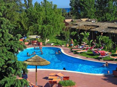 Piscine d'hôtel avec transats, parasols, arbres et vue sur la mer en arrière-plan.