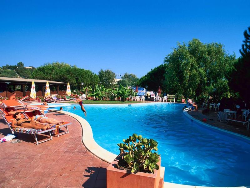 Grande piscine extérieure avec chaises longues par une journée ensoleillée.