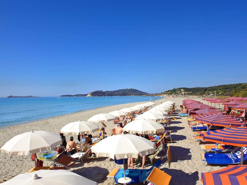 Plage avec parasols blancs et chaises longues au bord de la mer bleue claire sous un ciel dégagé.