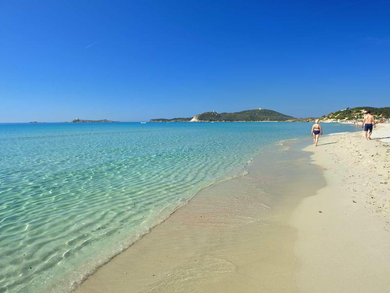 Ciel bleu clair au-dessus d'une plage de sable calme et en pente douce avec quelques personnes.