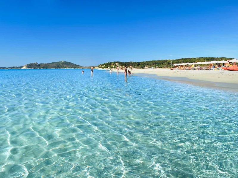 Mer turquoise claire avec plage de sable blanc et côte étendue sous ciel bleu.