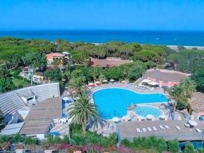 Große Poolanlage umgeben von Gebäuden und üppigem Grün mit Blick auf das blaue Meer im Hintergrund.