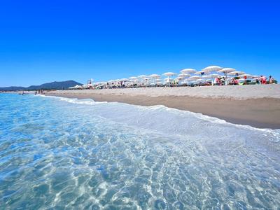 Klarer Ozean trifft auf sandigen Strand unter strahlend blauem Himmel mit weißen Sonnenschirmen.