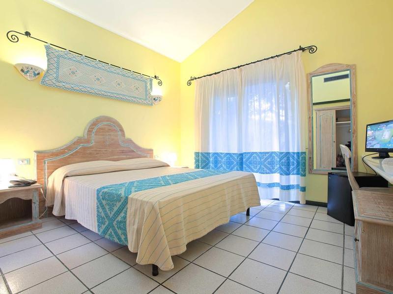 Helles Schlafzimmer mit großem Bett, hellen Wänden, Fliesenboden und Balkon mit Gardinen.