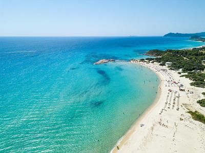 Rozlehlá písečná pláž s tyrkysovou vodou a zelenou vegetací v pozadí.