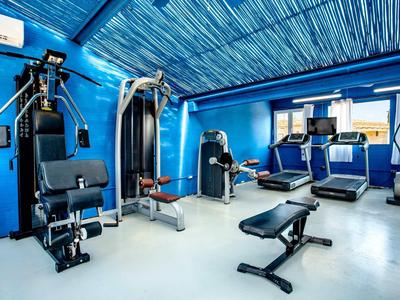 Light blue gym with various exercise machines and three treadmills by windows.