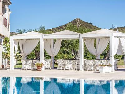 White pavilions with curtains by the pool in front of green hills under a clear sky.