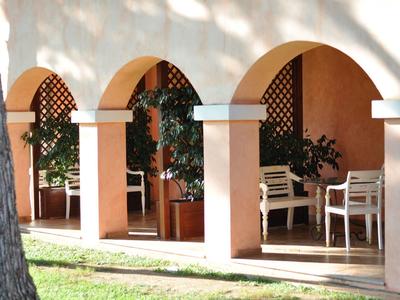 Overdekt terras met boogopeningen, witte stoelen en planten in daglicht