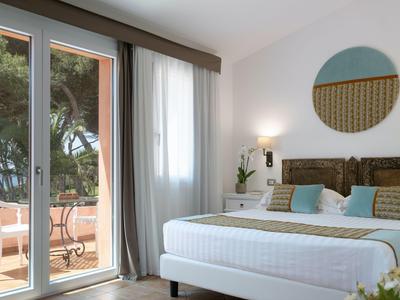 Lichte hotelkamer met groot bed, balkon en uitzicht op groen.