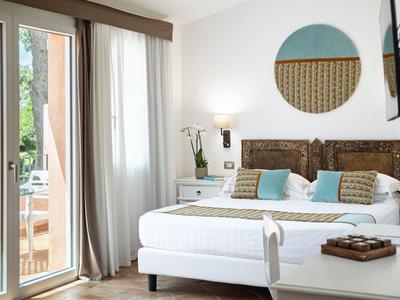 Lichte hotelkamer met tweepersoonsbed, kussens en balkon met uitzicht op groen.