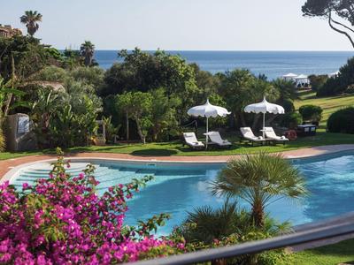 Zwembad met parasols en ligstoelen in tropische tuin met zeezicht.