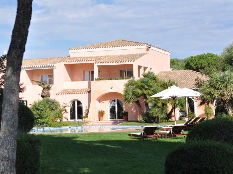 Large bright holiday home with pool and shaded loungers in the garden.