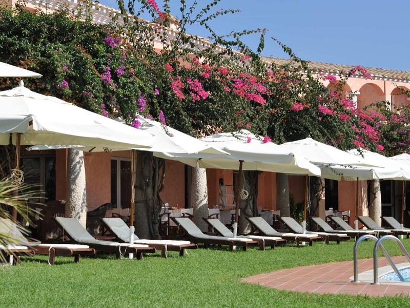 Row of lounge chairs with white umbrellas in front of flowering building and green lawn