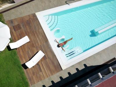 Widok z góry na basen z osobą w środku, otoczony drewnianym tarasem i leżakami.