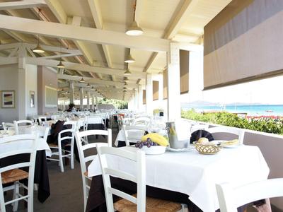 Zadaszony taras restauracyjny z białymi stołami i widokiem na morze.