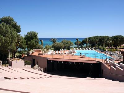 Basen hotelowy z leżakami, otoczony drzewami, z widokiem na niebieskie morze pod czystym niebem.