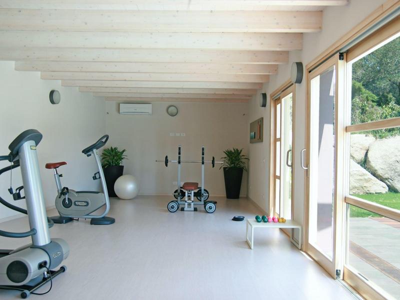 Jasna siłownia z urządzeniami treningowymi i dużymi przesuwnymi drzwiami na zewnątrz.