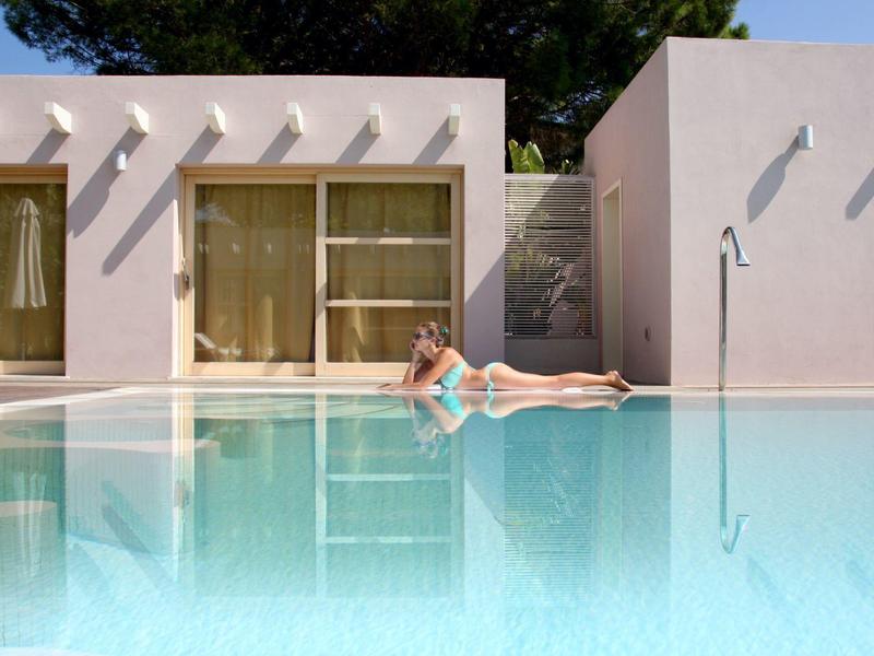 Kobieta odpoczywająca na brzegu basenu w nowoczesnym hotelu z białymi budynkami i zielonymi zasłonami.