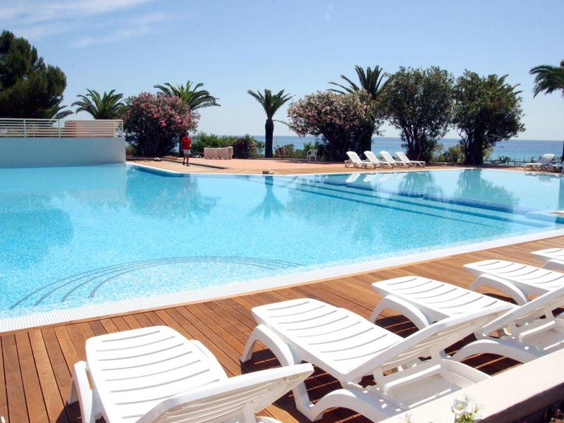 Duży basen na zewnątrz z białymi leżakami i drzewami w tle nad morzem.