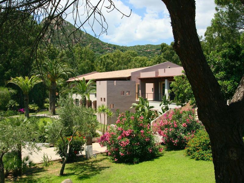 Dom w zielonym, kwitnącym ogrodzie z wzgórzami w tle.