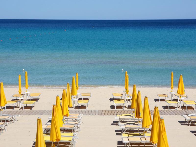 Plaża z żółtymi parasolami i leżakami z widokiem na niebieskie morze i czyste niebo.