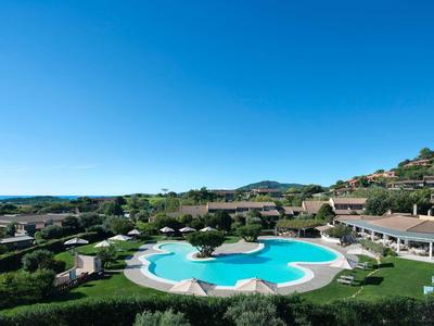 Une grande piscine d'hôtel dans un paysage verdoyant sous un ciel bleu clair.
