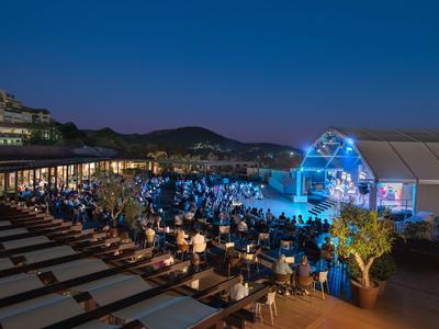 Un hôtel de plage éclairé avec des clients la nuit et une tente illuminée sur la plage.