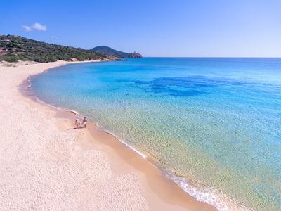 Une plage de sable tranquille avec une eau bleu-vert claire et peu de monde sous un ciel dégagé.
