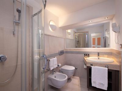 Salle de bain moderne d'hôtel avec douche, deux lavabos, bidet et carrelage clair.