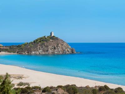 Plage de sable blanc avec eau bleue claire et une petite île avec un phare.
