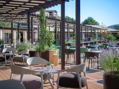 Espace extérieur moderne d'un hôtel avec mobilier de terrasse et plantes sous un ciel clair.