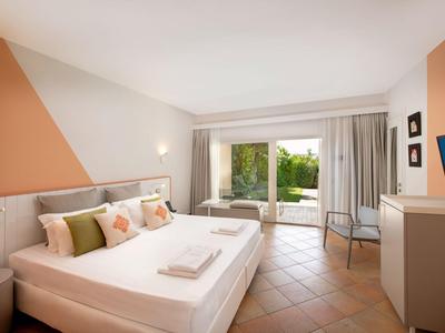 Chambre d'hôtel lumineuse avec lit double, porte de terrasse et vue sur le jardin.