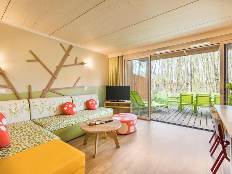 Bright living room with green sofa, mushroom cushions, and terrace with green chairs in forest