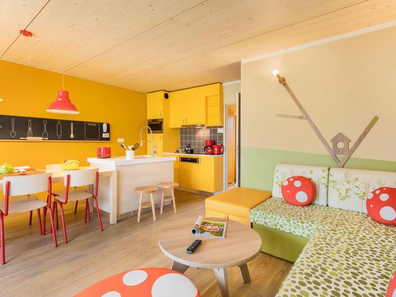 Bright, colorful kitchen and living area with yellow walls, red chairs, and patterned sofas.