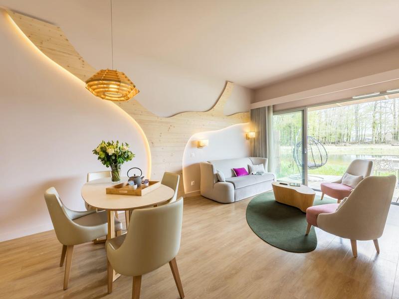 Modern living room with dining area, sofas, and large window overlooking greenery.