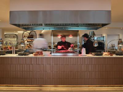 Küchenbereich mit drei Personen, großem Dunstabzug und brauner Kacheltheke in Restaurant.