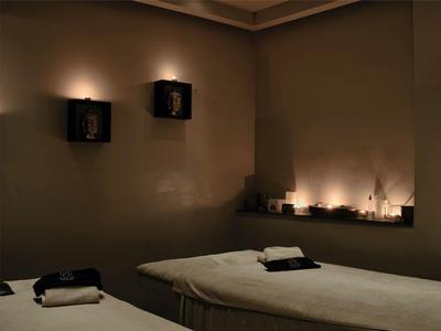 Dunkler Raum mit zwei Massageliegen und gedämpfter Beleuchtung an Wänden und Regalen.