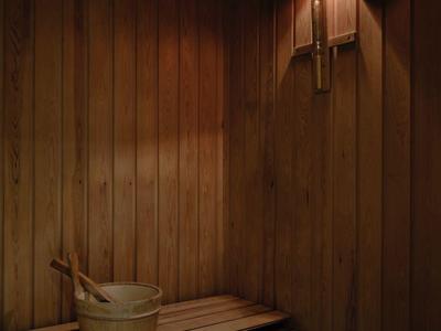 Holzsauna mit Sitzbank, Holzeimer und Schöpfkelle, warme Beleuchtung an der Wand.