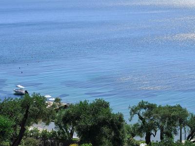 Klares Meer mit Inseln im Hintergrund, im Vordergrund Bäume und ein Spielplatz mit Schaukeln und Kletterhaus.