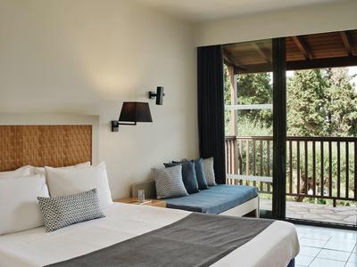 Helles Schlafzimmer mit großem Bett, Sitzbank, schwarzen Vorhängen und Balkon mit Holzgeländer.