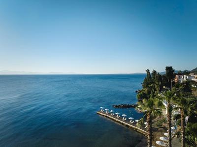 Kustzicht met blauwe zee, heldere lucht en een paar ligstoelen bij de kust naast palmbomen.