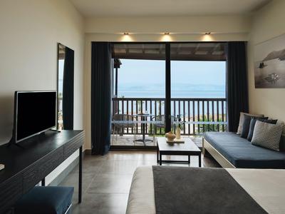 Modern hotelkamer met tweepersoonsbed, bank, tv en balkon met uitzicht op zee.