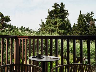 Kleiner runder Tisch mit Tasse und Buch auf Holzterrasse vor grünen Bäumen und blauem Himmel.